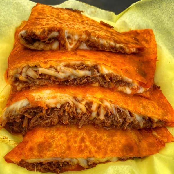 Four birria quesadillas with melted cheese and shredded meat, served on yellow paper.