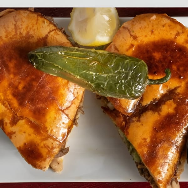 Two golden-brown Birrieria Esquivel quesabirrias with a grilled jalapeño and lemon wedge on a white plate.